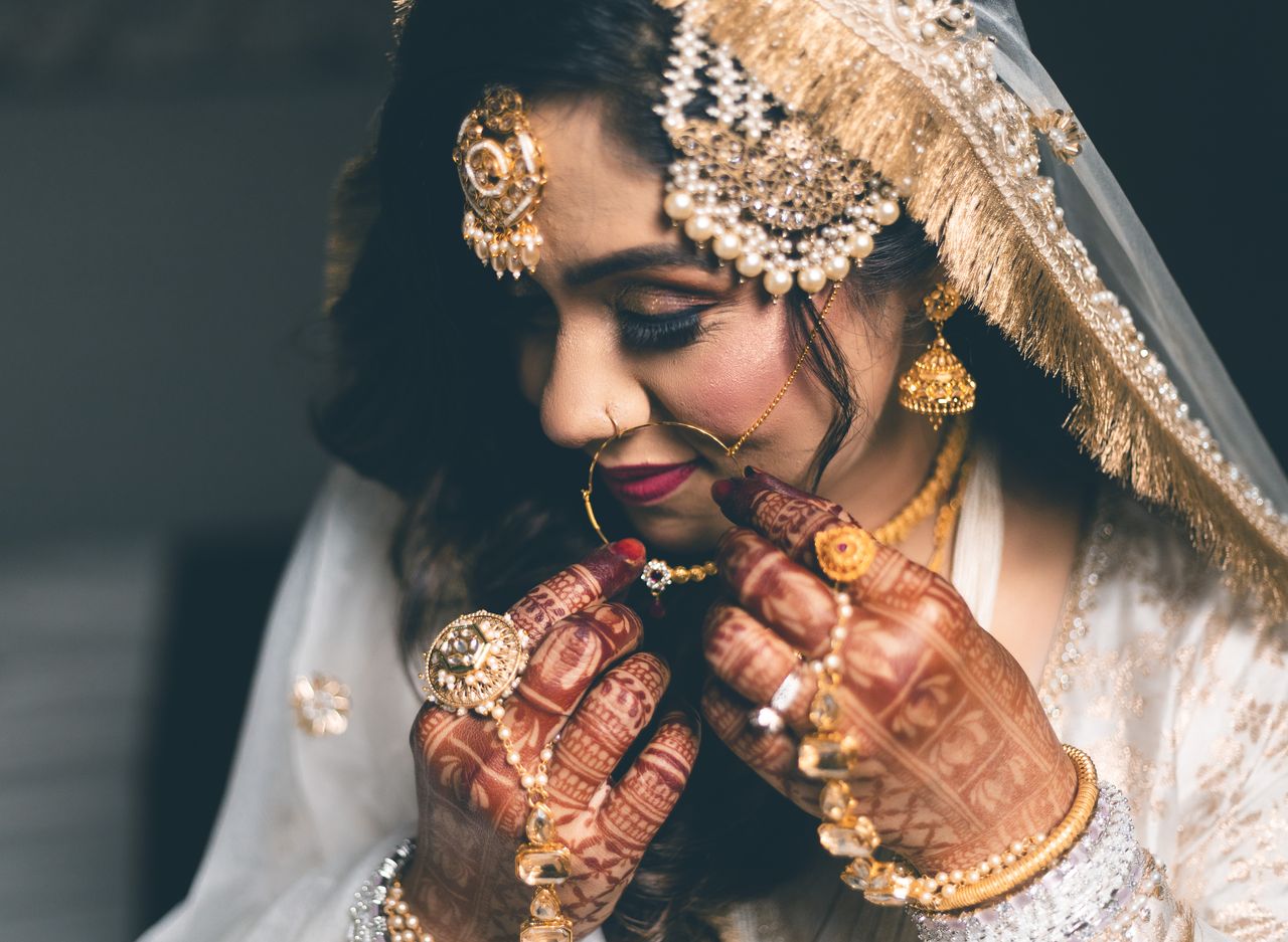 Close-up of a bride adjusting her nath, hands covered in mehendi and rings