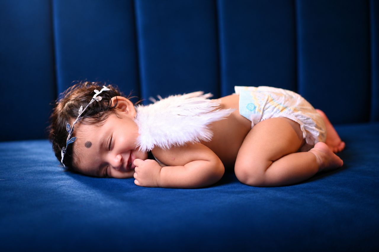 A baby with small angel wings sleeping on a deep blue bed