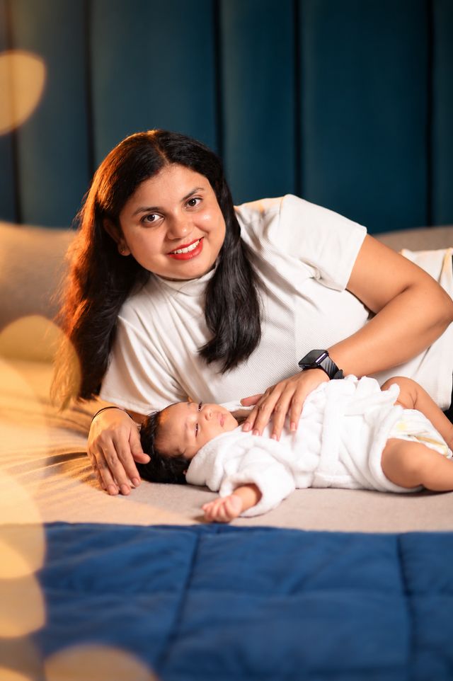 A mother lies beside her baby on the bed, smiling down at her