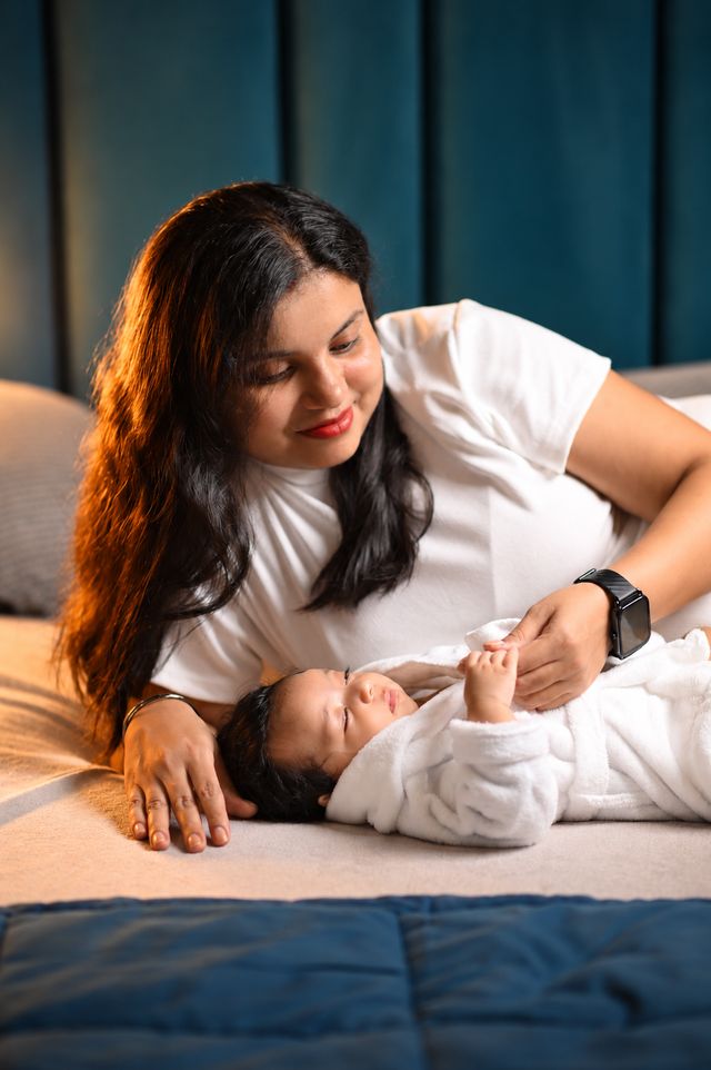 A mother gazes at her baby lying on a white blanket
