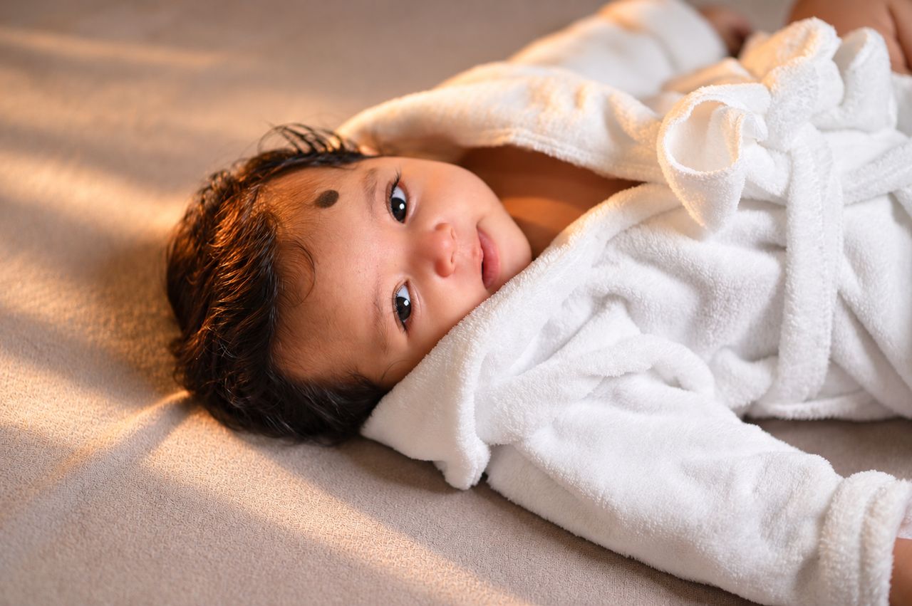 A baby in a white robe looking up at the camera