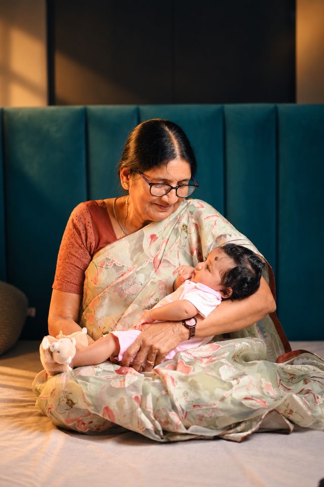 A grandmother in a printed saree cradles her granddaughter