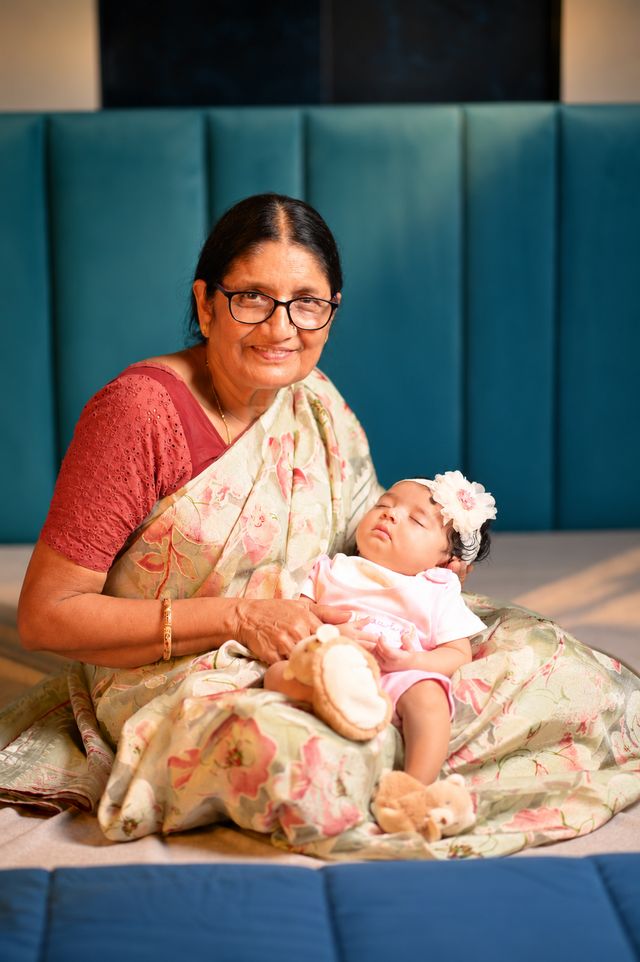 A grandmother sits with her granddaughter on her lap, smiling at the camera
