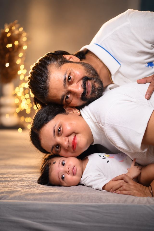Father, mother and baby stacked cheek to cheek on the bed, all smiling