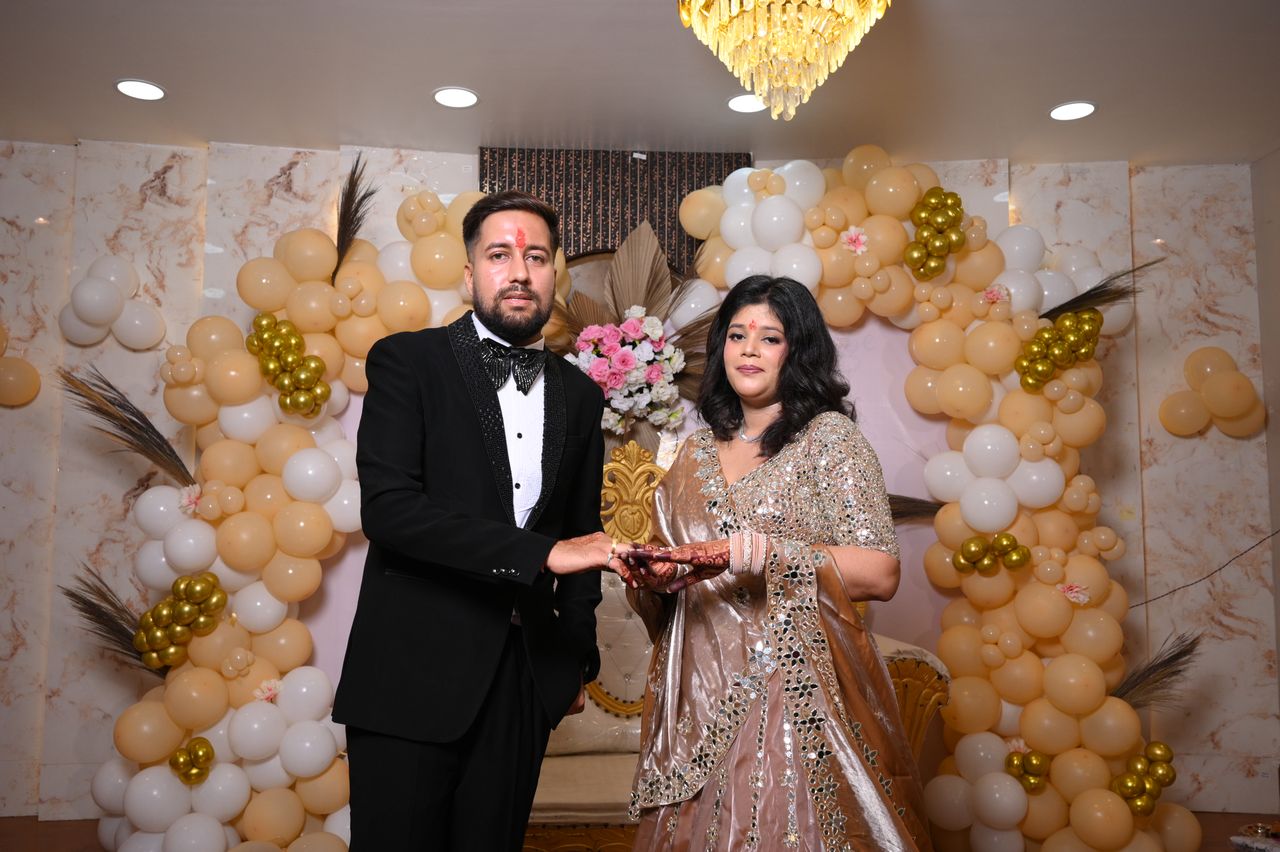 A couple exchanging rings in front of a balloon and floral backdrop