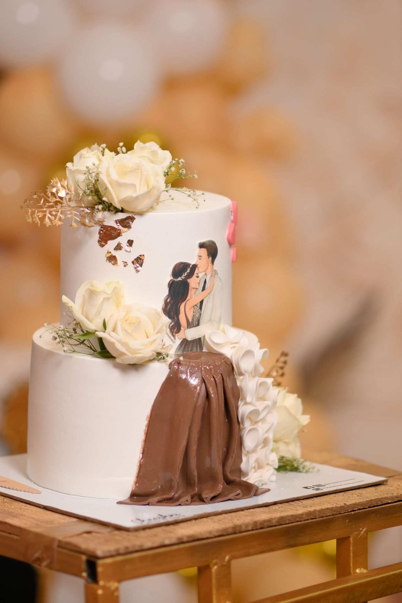 A two-tier engagement cake with white roses and a hand-painted couple