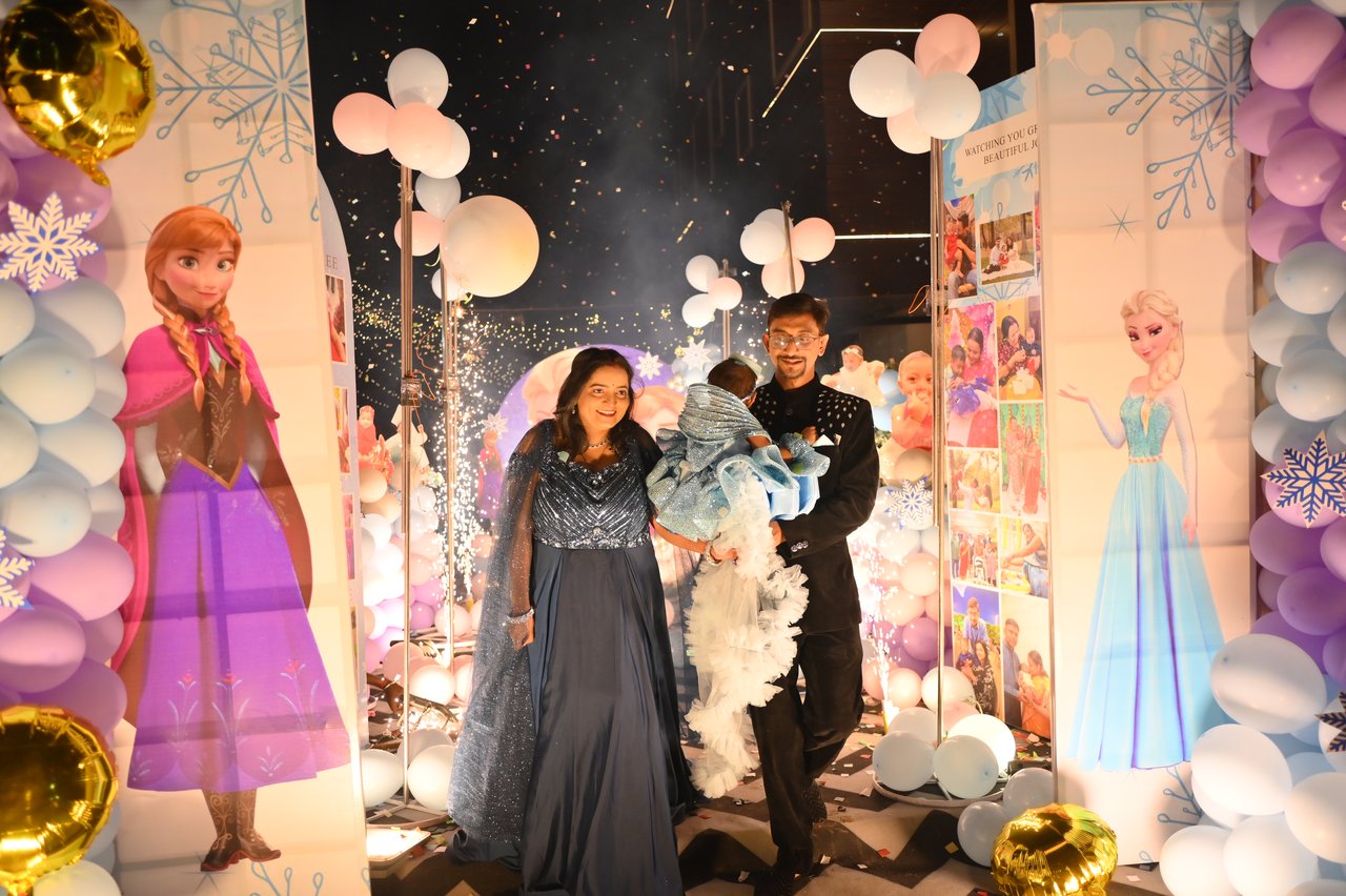 A couple with their baby stand before a castle-themed birthday stage