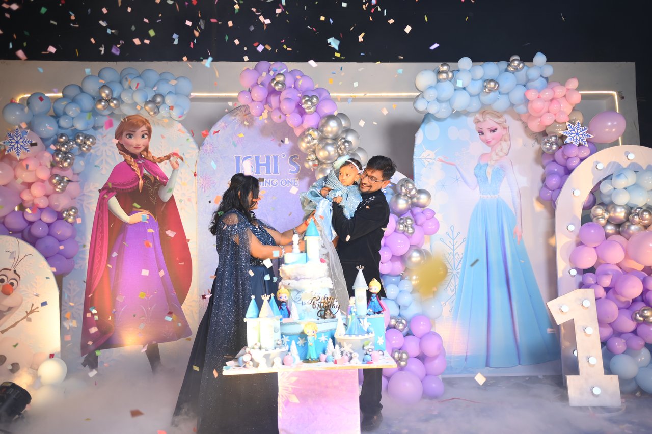 The birthday family poses beside the cake on a decorated stage