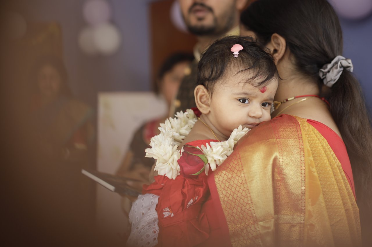 A baby in red looks over her mother's shoulder at the annaprashan