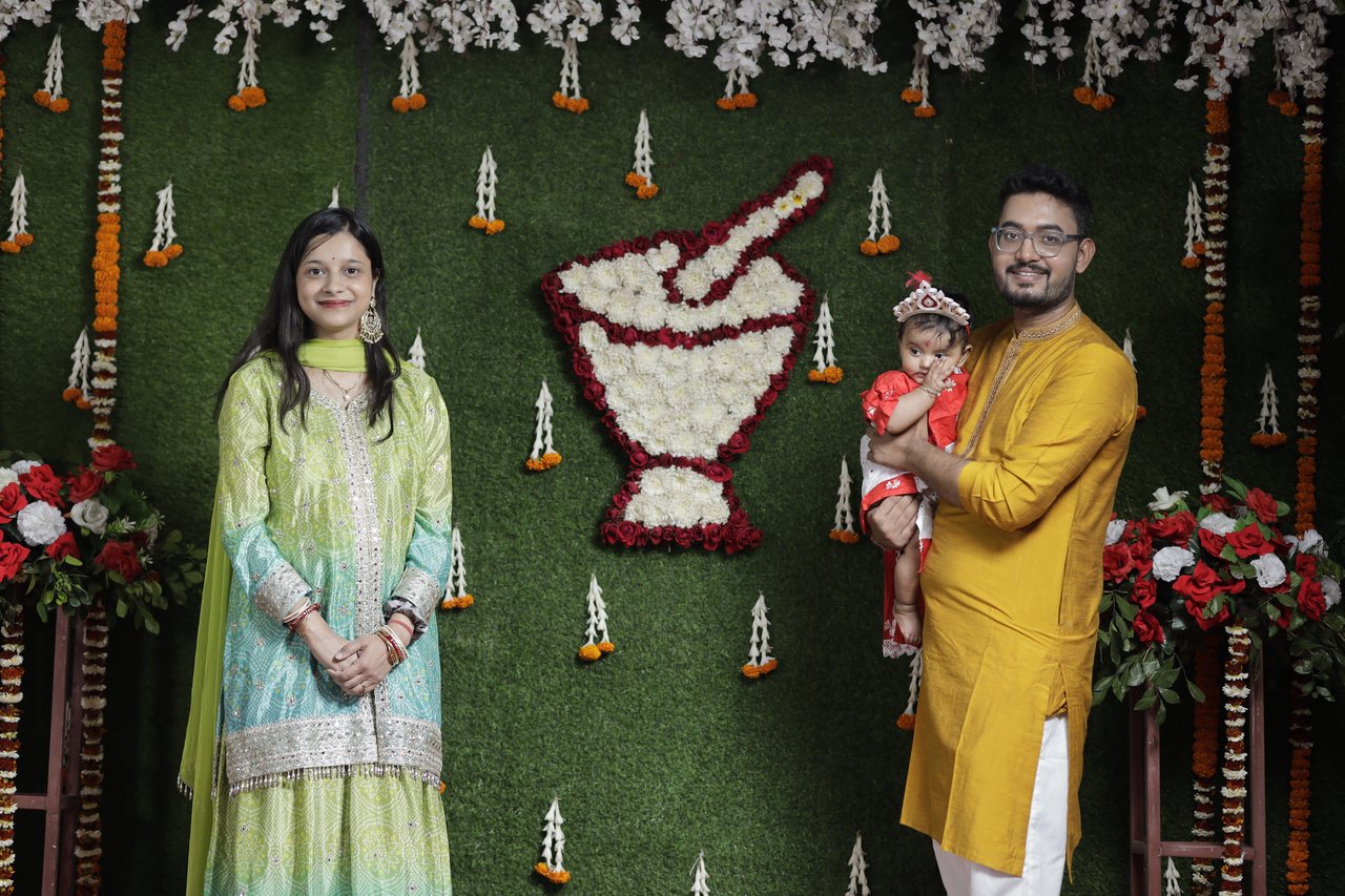Parents and their baby stand beside a floral backdrop