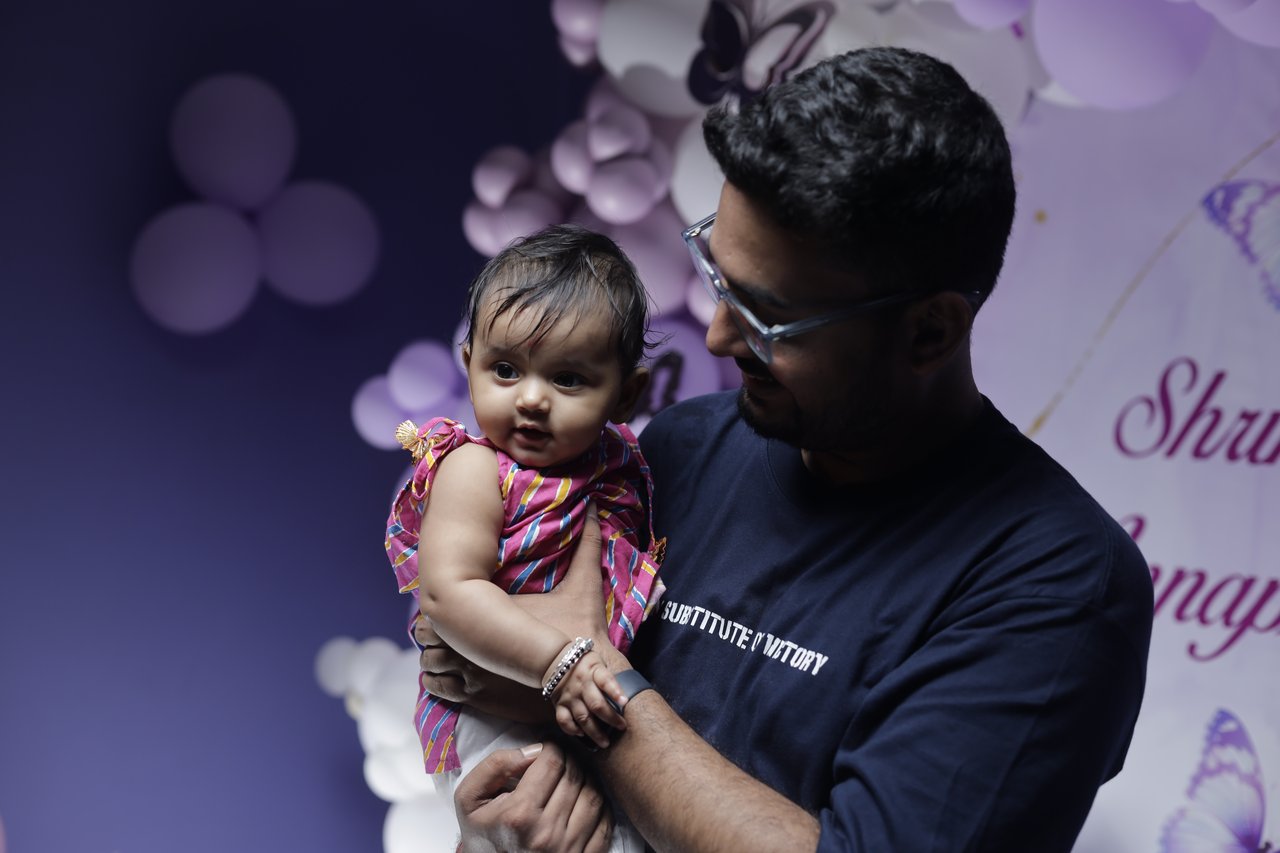 A father holds his baby daughter in front of a lilac balloon backdrop