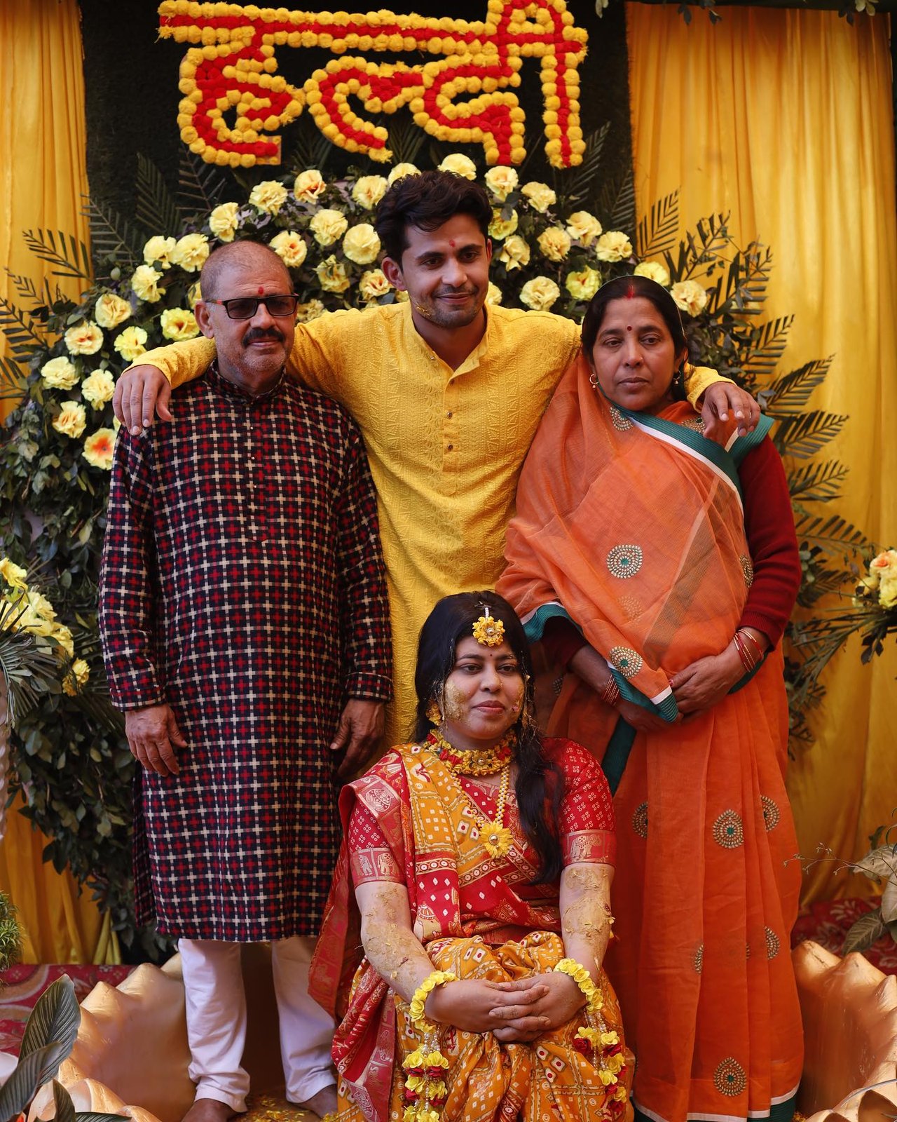A family portrait at a haldi beneath a marigold sign