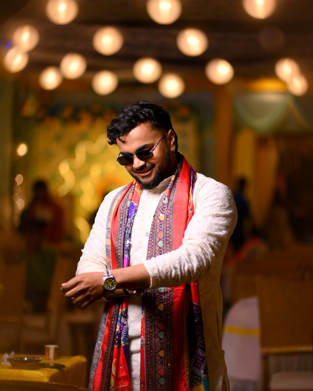 A groom in sunglasses and a printed dupatta under warm lights