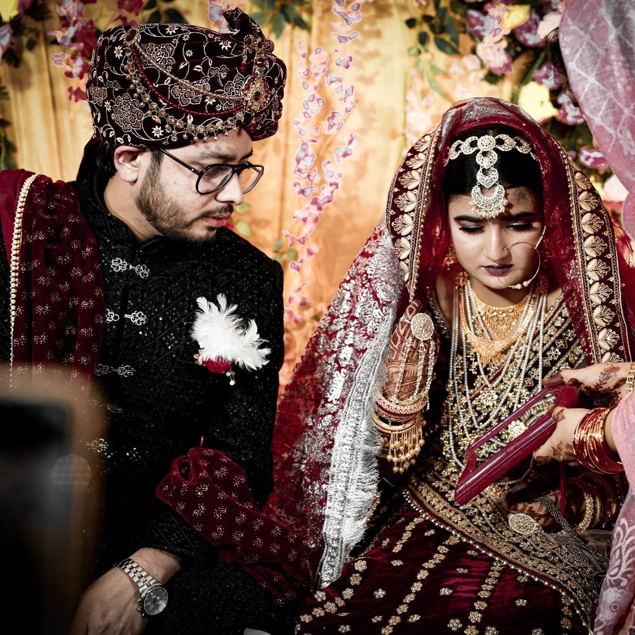 Bride and groom in maroon wedding outfits share a quiet moment