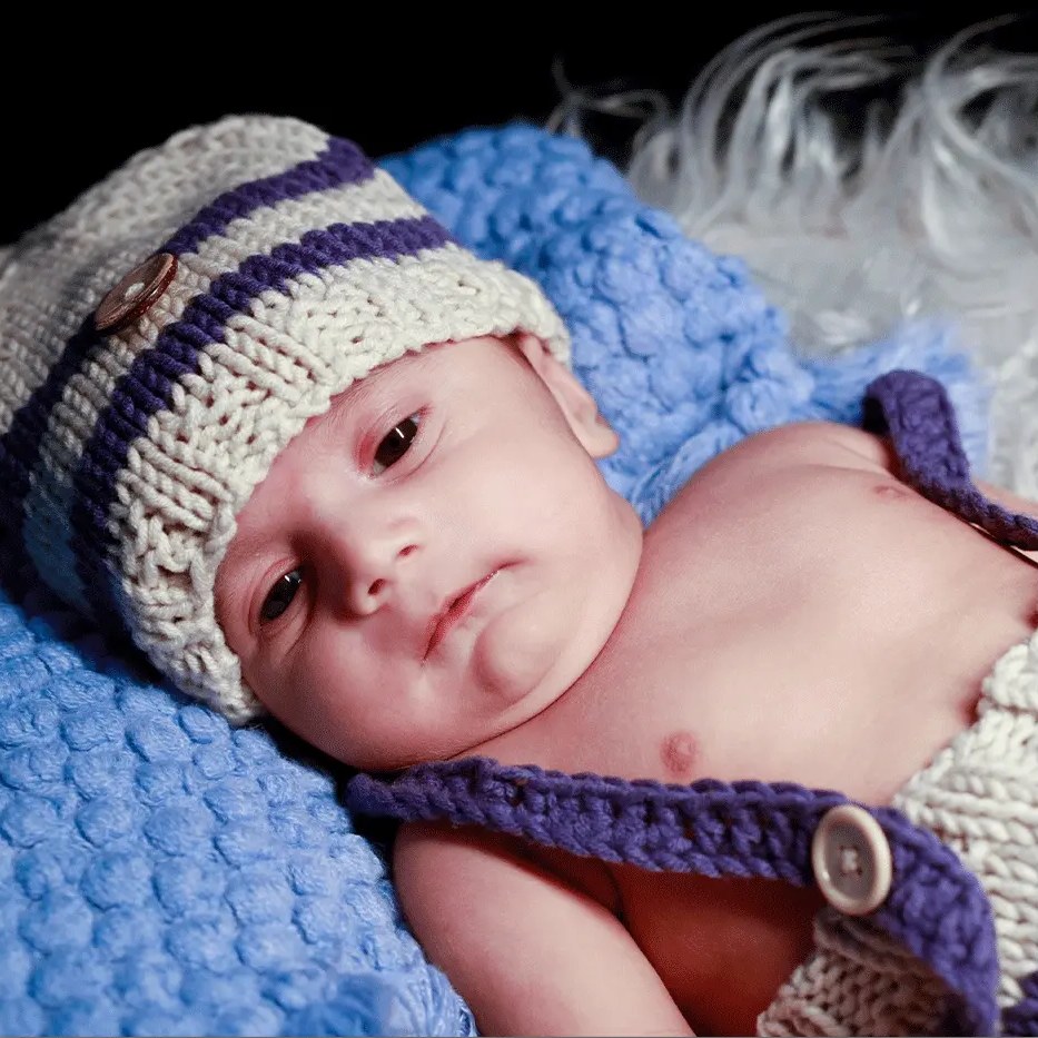 A baby in a striped knitted hat lies on a blue blanket