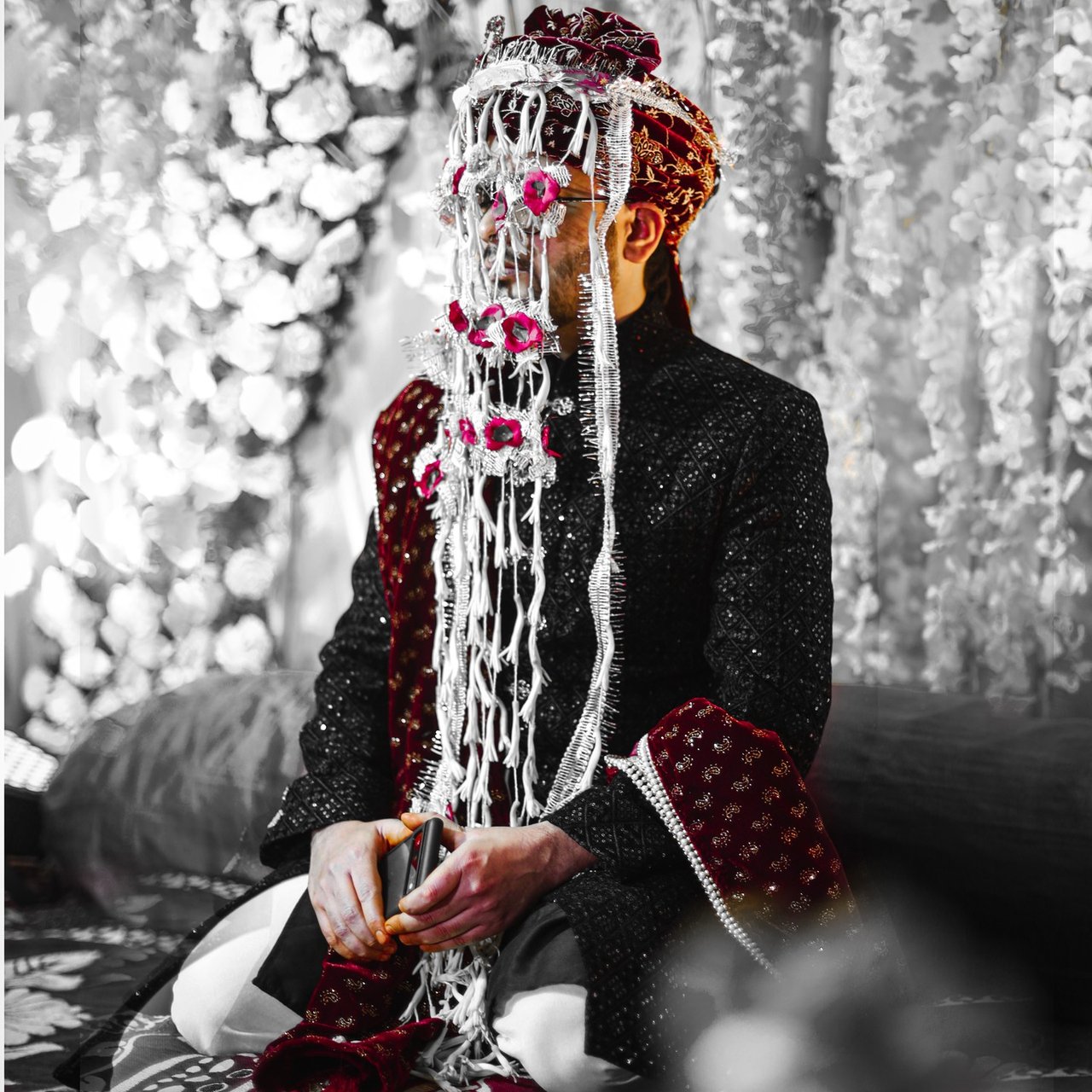 Black and white portrait of a groom wearing a floral sehra