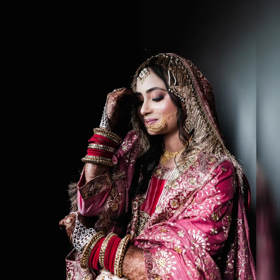 A bride in a pink dupatta adjusts her jewellery