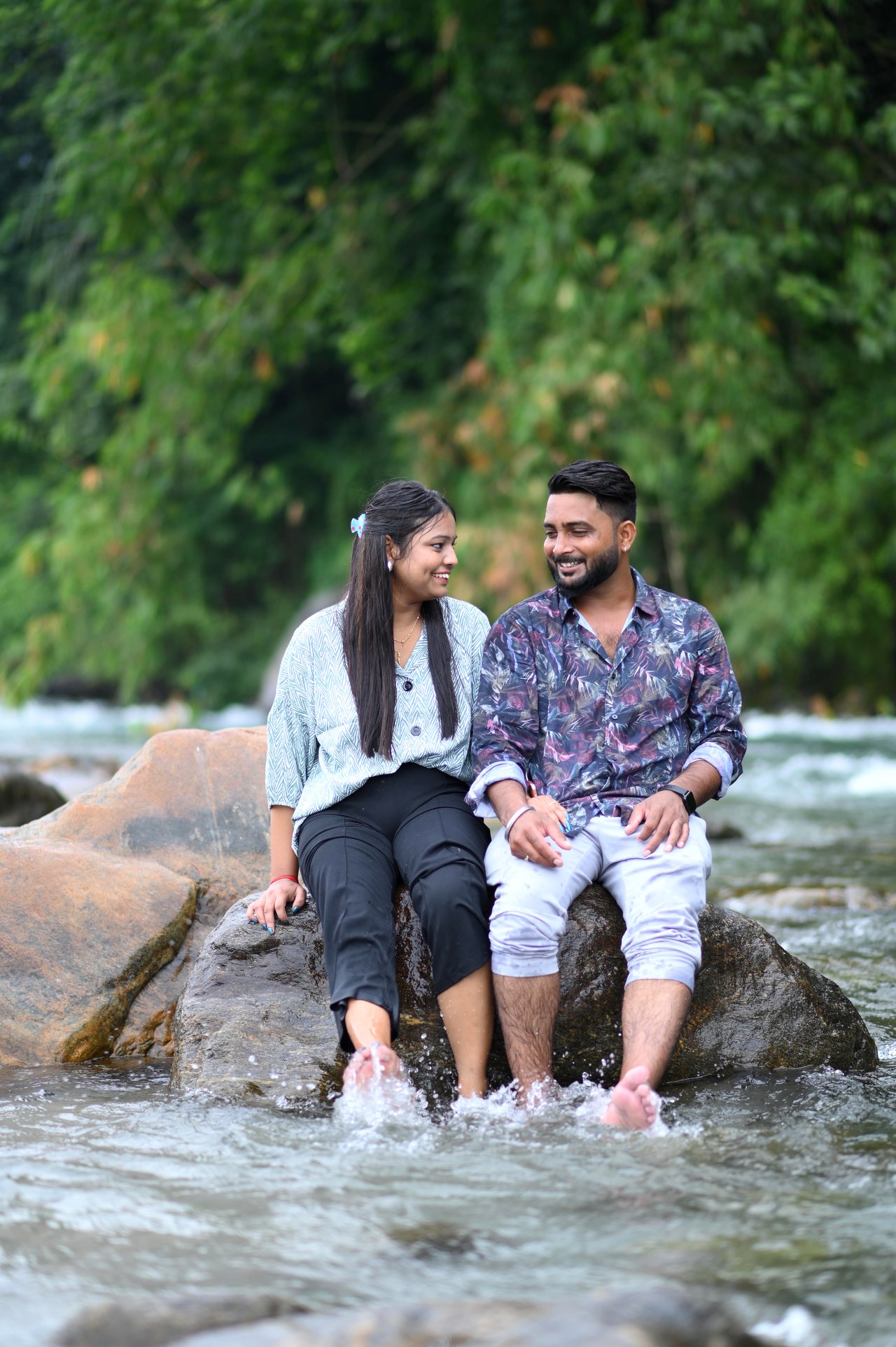 A couple sit together on a boulder beside a waterfall