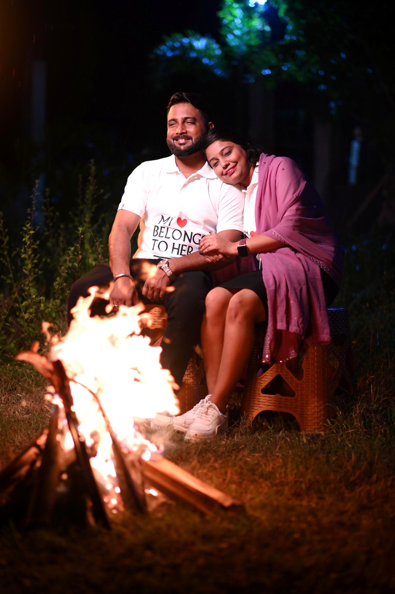 A couple laugh beside a campfire at night