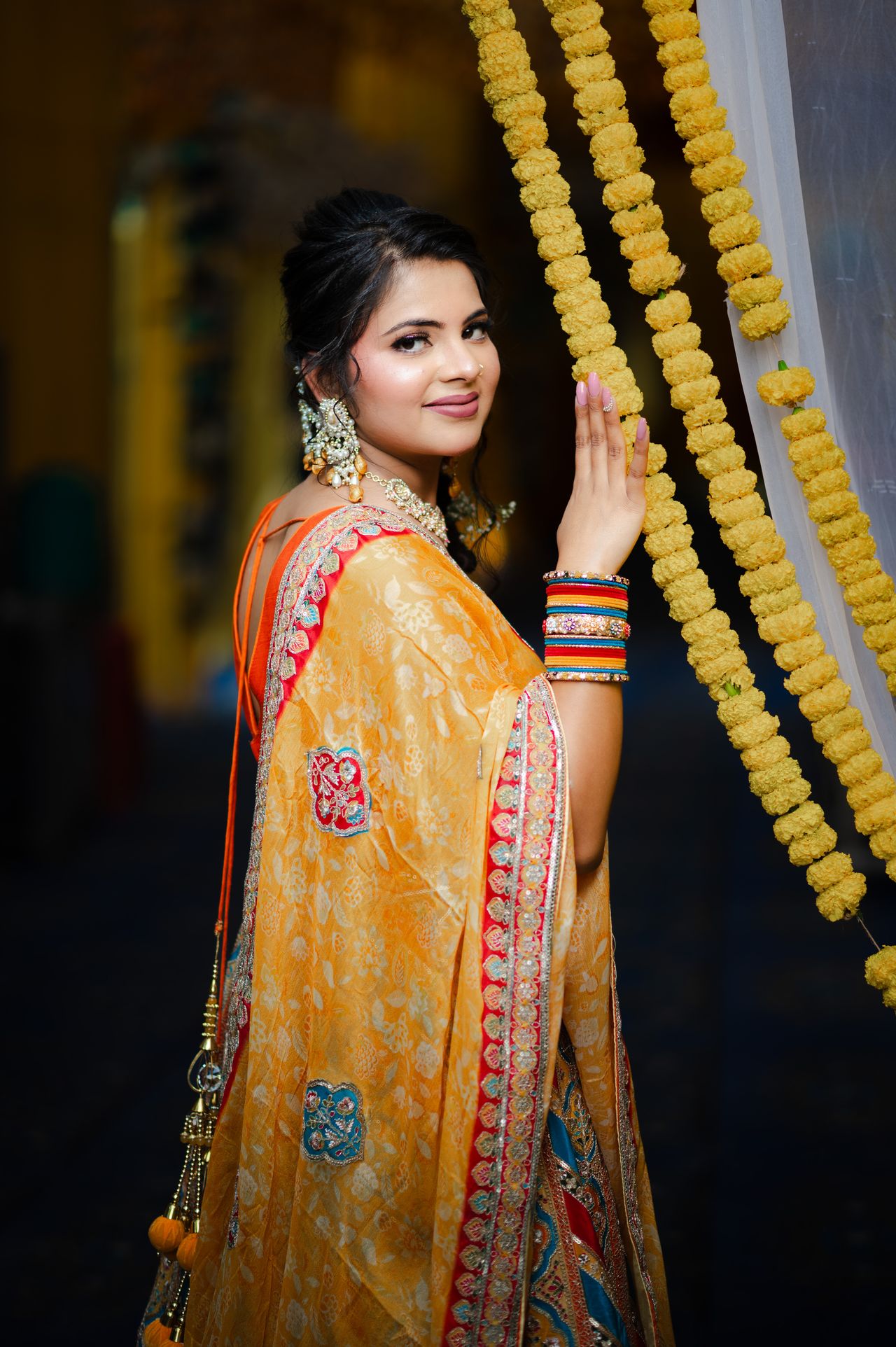 Bride in a marigold dupatta touching a garland of yellow flowers at her haldi