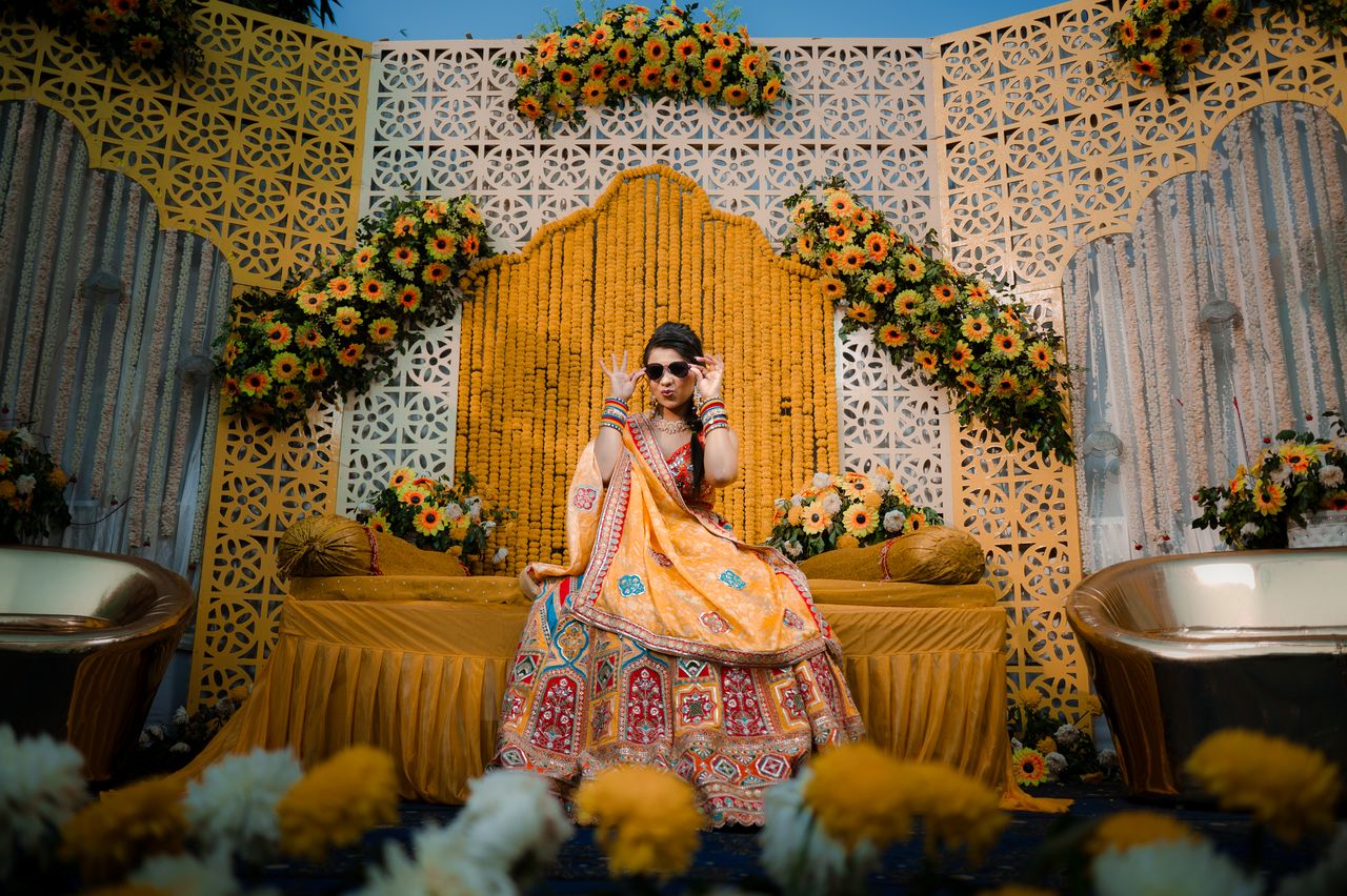 Bride seated on a haldi stage of marigolds and carved white screens