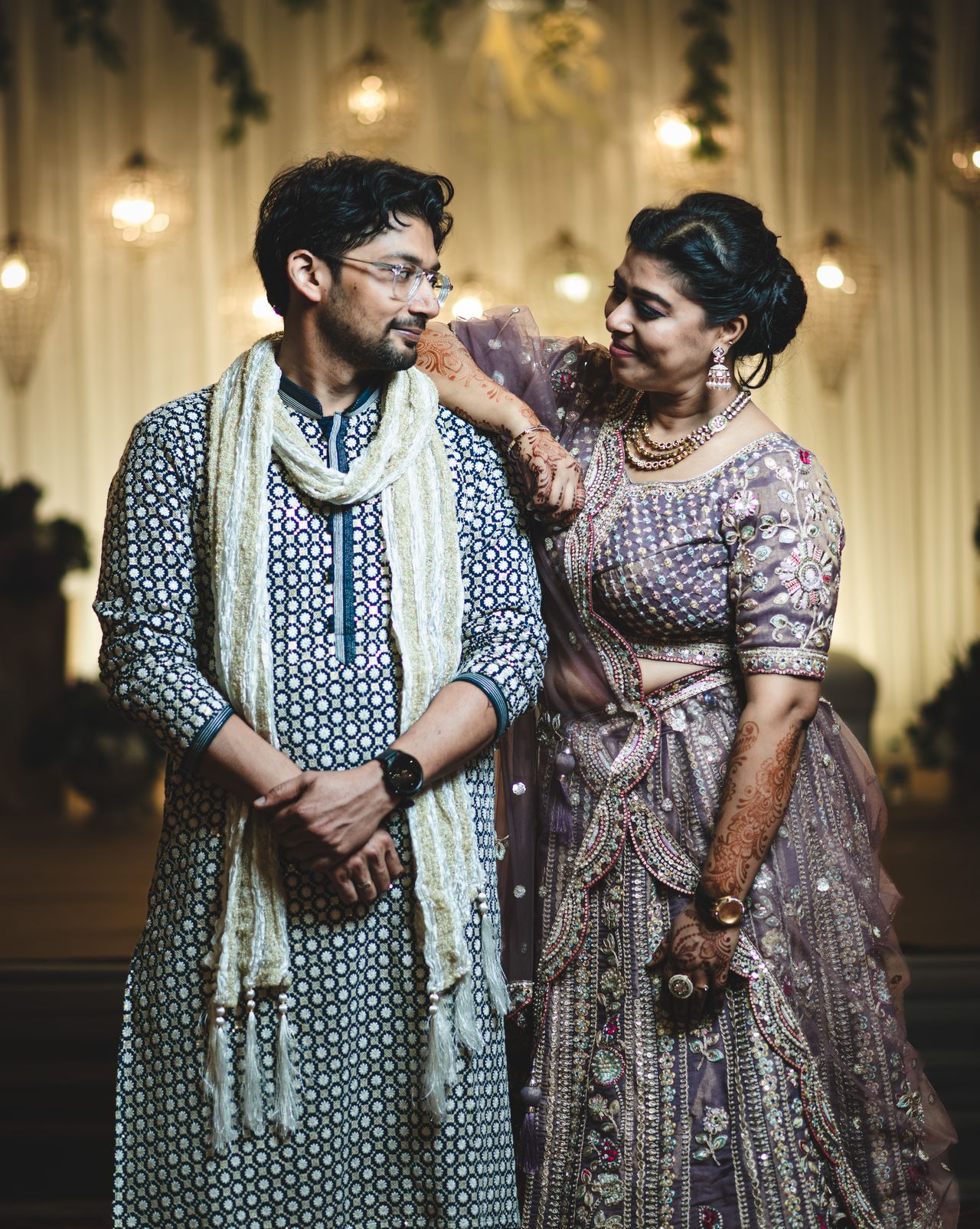 A man and a woman in festive attire share a warm moment beneath hanging lanterns