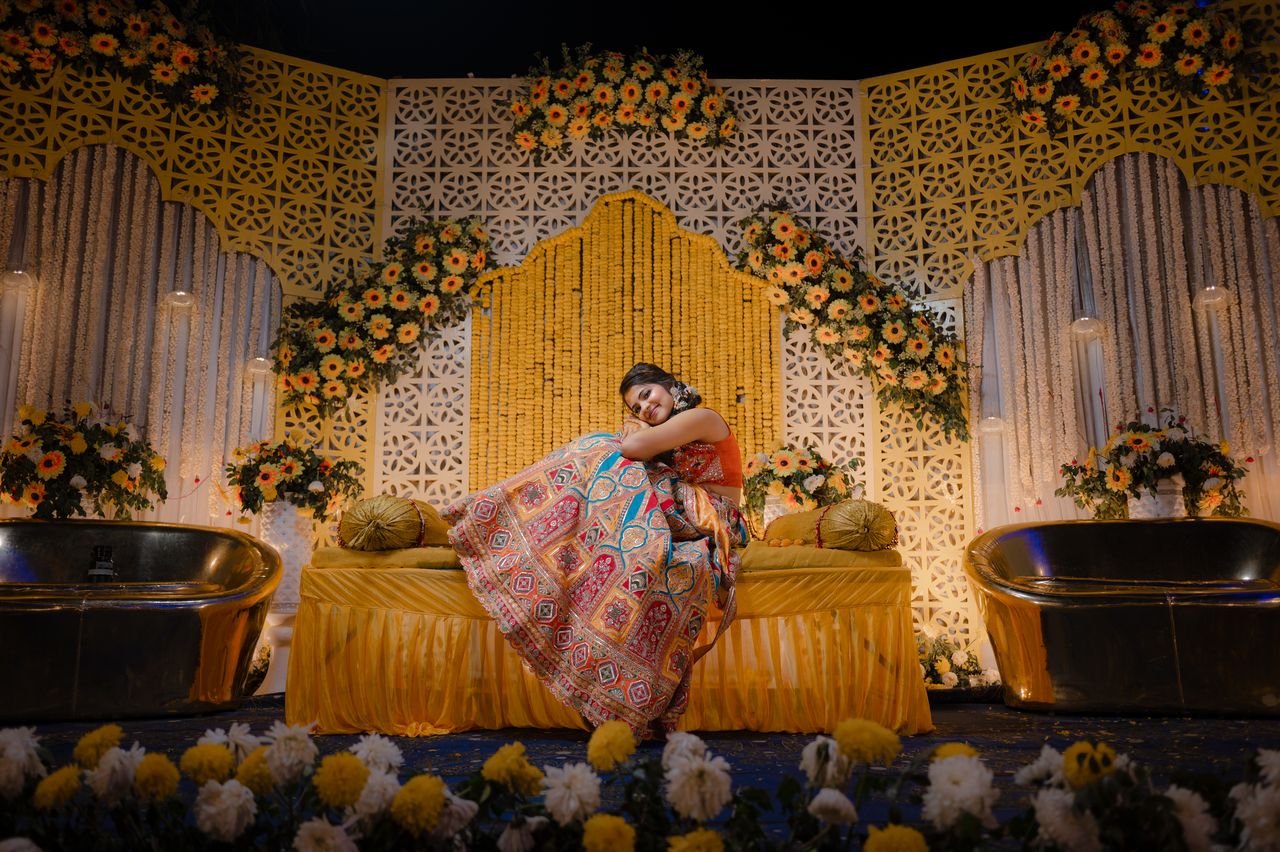 Bride reclining on a haldi stage of marigolds and carved screens, warm evening light