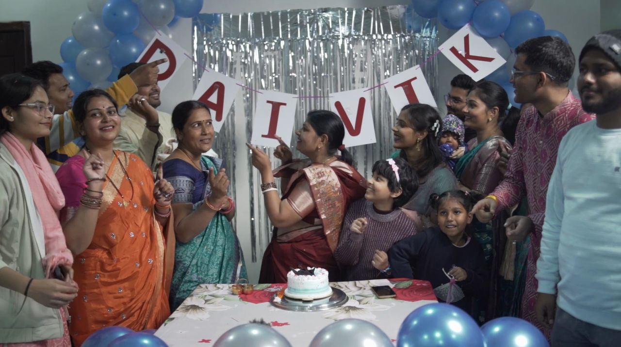 Family gathered around a cake at a baby's naming celebration with balloons