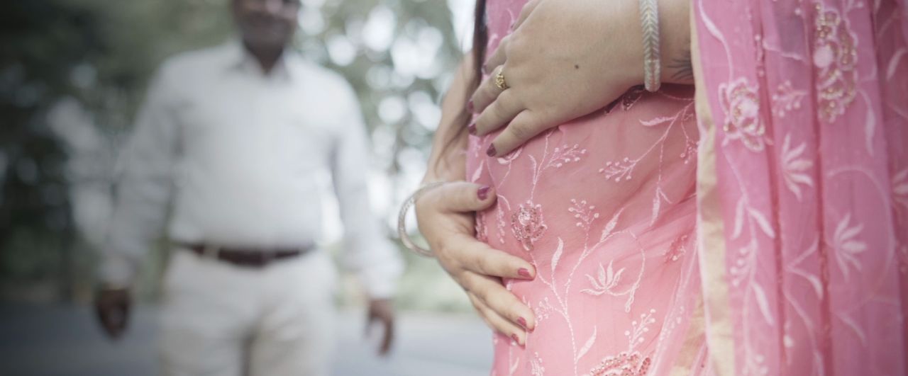 Hands resting on a baby bump in a pink embroidered kurta