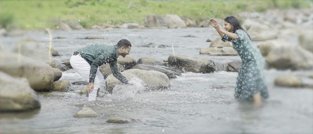 A couple splashing each other while crossing a rocky river